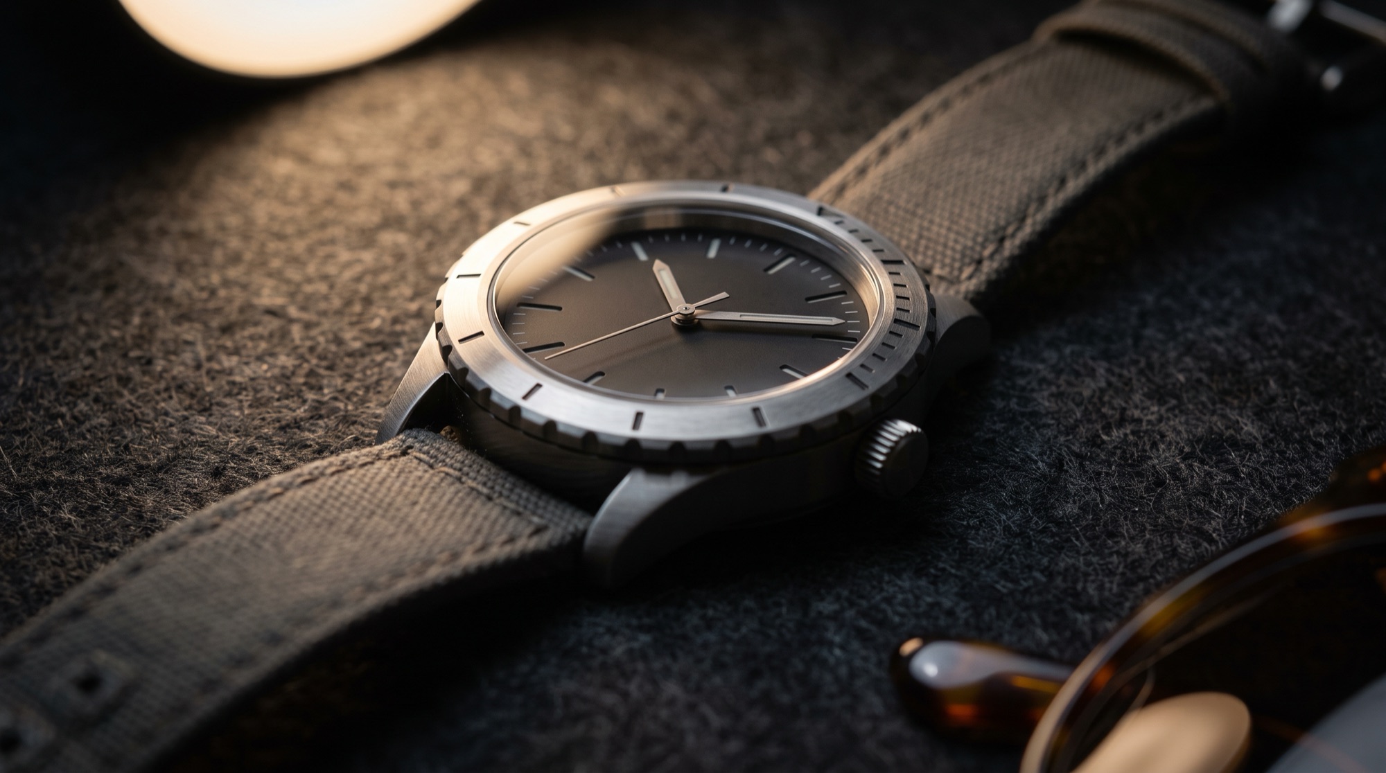 A steel field watch under a single spotlight on dark felt.